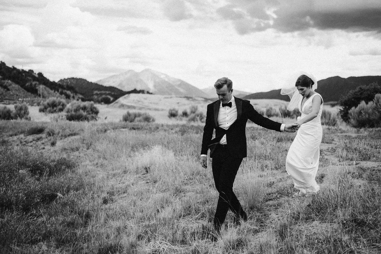 bride and groom walking in field below mountain peak